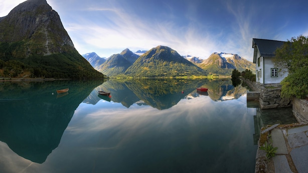 A tranquil lake with boats, a stone house, and mountains in the background. - Hjelle Hotel (Stryn)