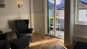 A room with a large window offering a mountain view, a black armchair, a white chair, and a chandelier. - Hjelle Hotel (Stryn)