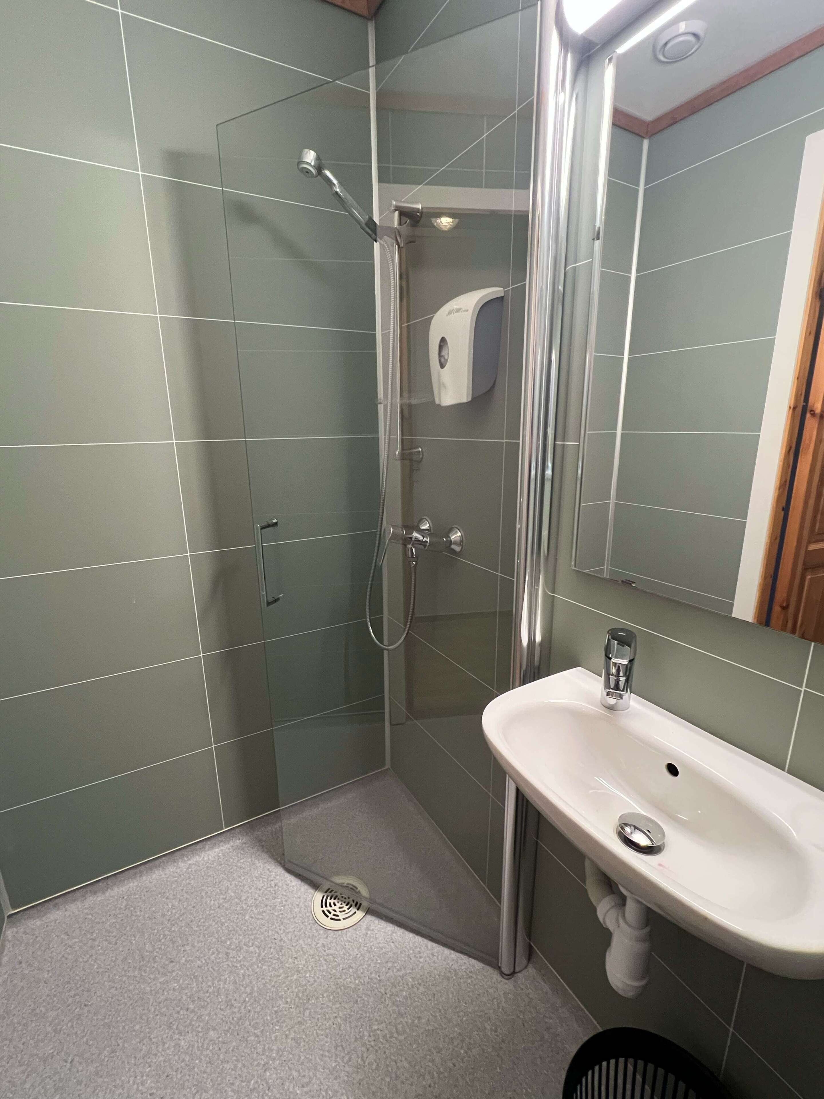 A bathroom with a glass-enclosed shower, a white sink, and a hand soap dispenser.