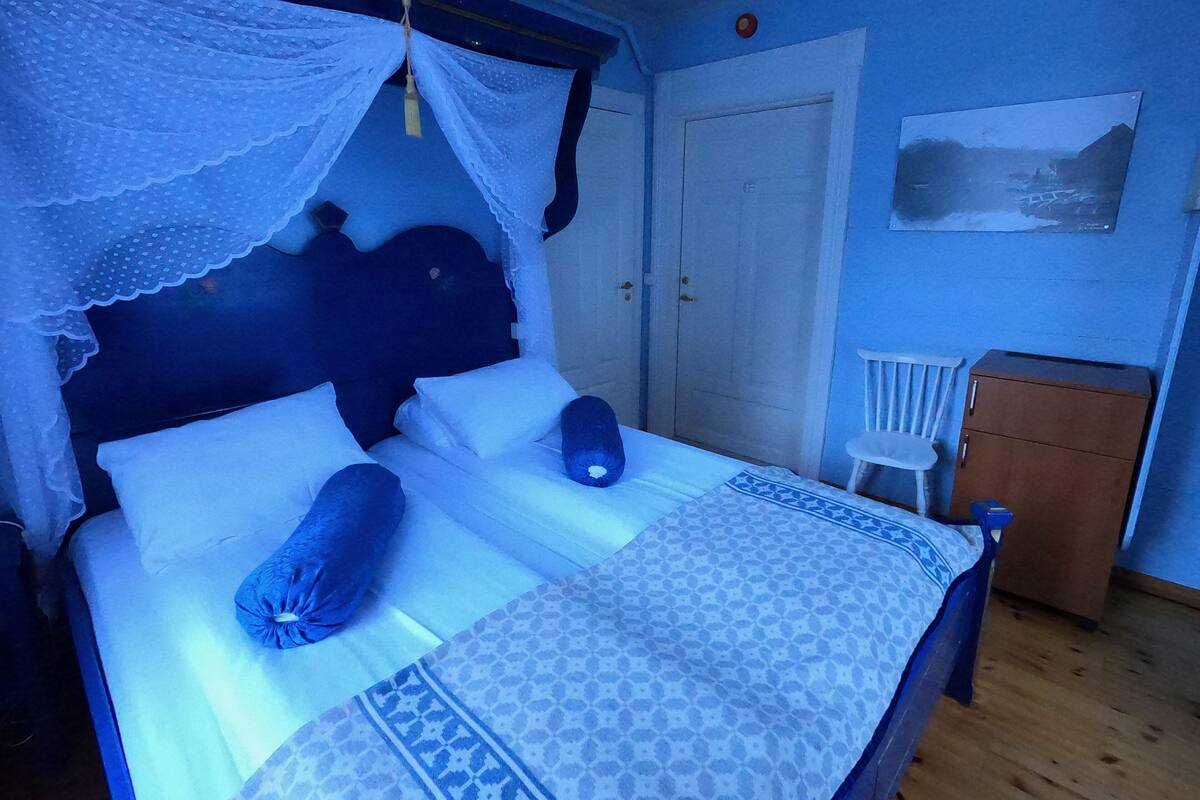 Una cama con dosel, una mesita de noche, una silla y un armario en una habitación con paredes azules.