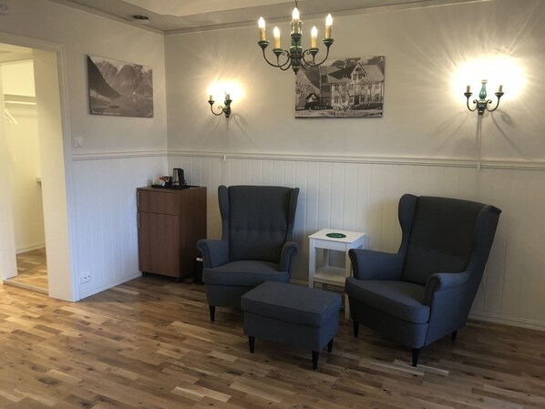 Una habitación con dos sillones, una mesita pequeña y un aparador. Hay apliques en la pared y un candelabro.