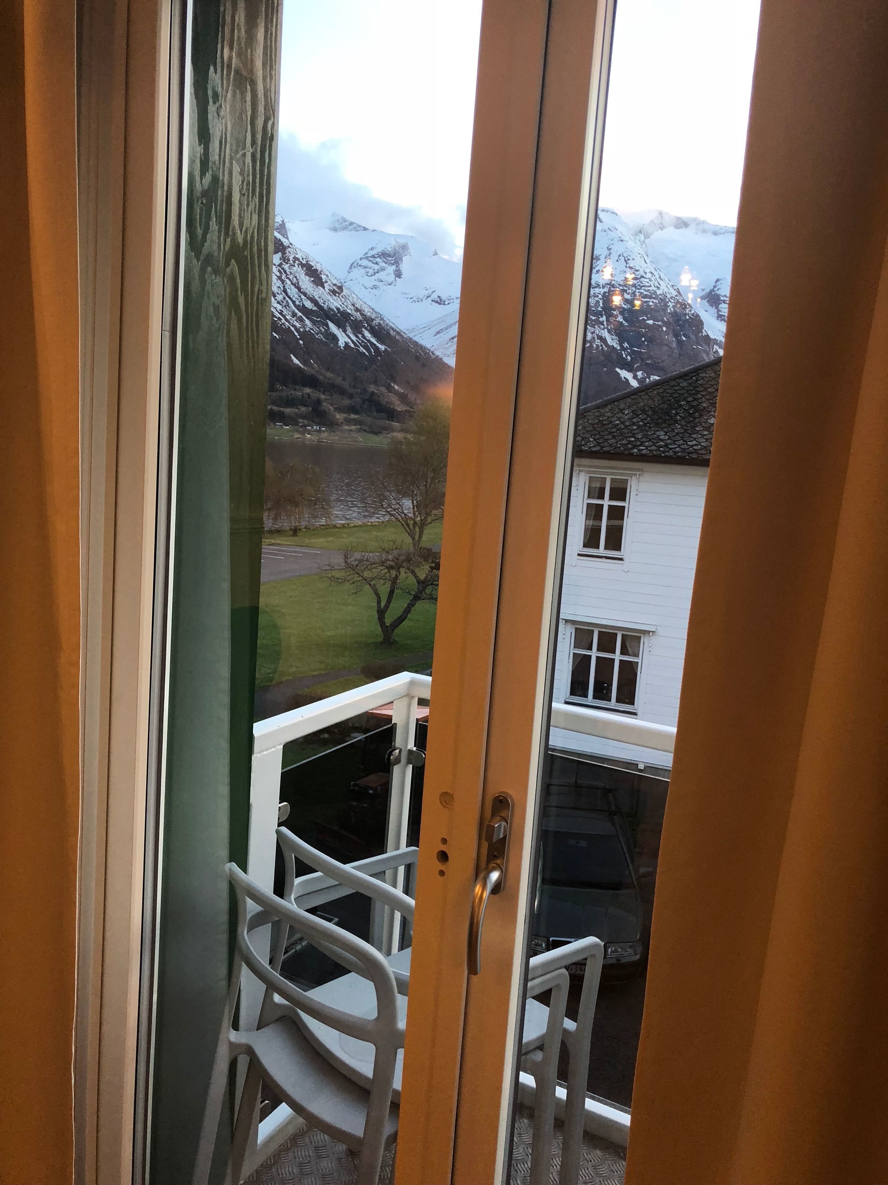 Blick vom Balkon mit Metallgeländer auf eine verschneite Landschaft mit Bergen und einem weißen Gebäude im Hintergrund.
