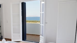 Een hotelkamer met een bed en uitzicht op zee door een geopende deur, plus een balkon.