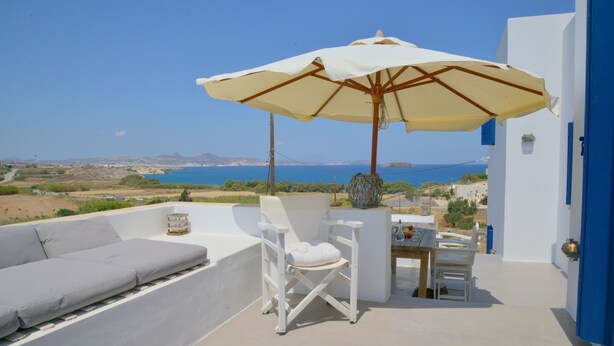 Een terras met een witte bank, een tafel met stoelen en een parasol.