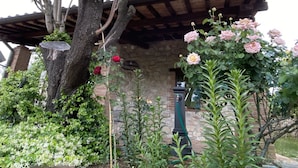 A stone building with a wooden roof, surrounded by lush greenery and flowering plants. - Lisetta Holiday homes - Ladybug House - Family House (Perugia)