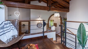 A rustic interior with exposed wooden beams, a wooden chair with a patterned blanket, a staircase with a metal railing, and a large green plant. - Lisetta Holiday homes - Ladybug House - Family House (Perugia)