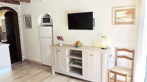 A compact kitchen with a microwave, refrigerator, and a flat-screen TV mounted on the wall.
