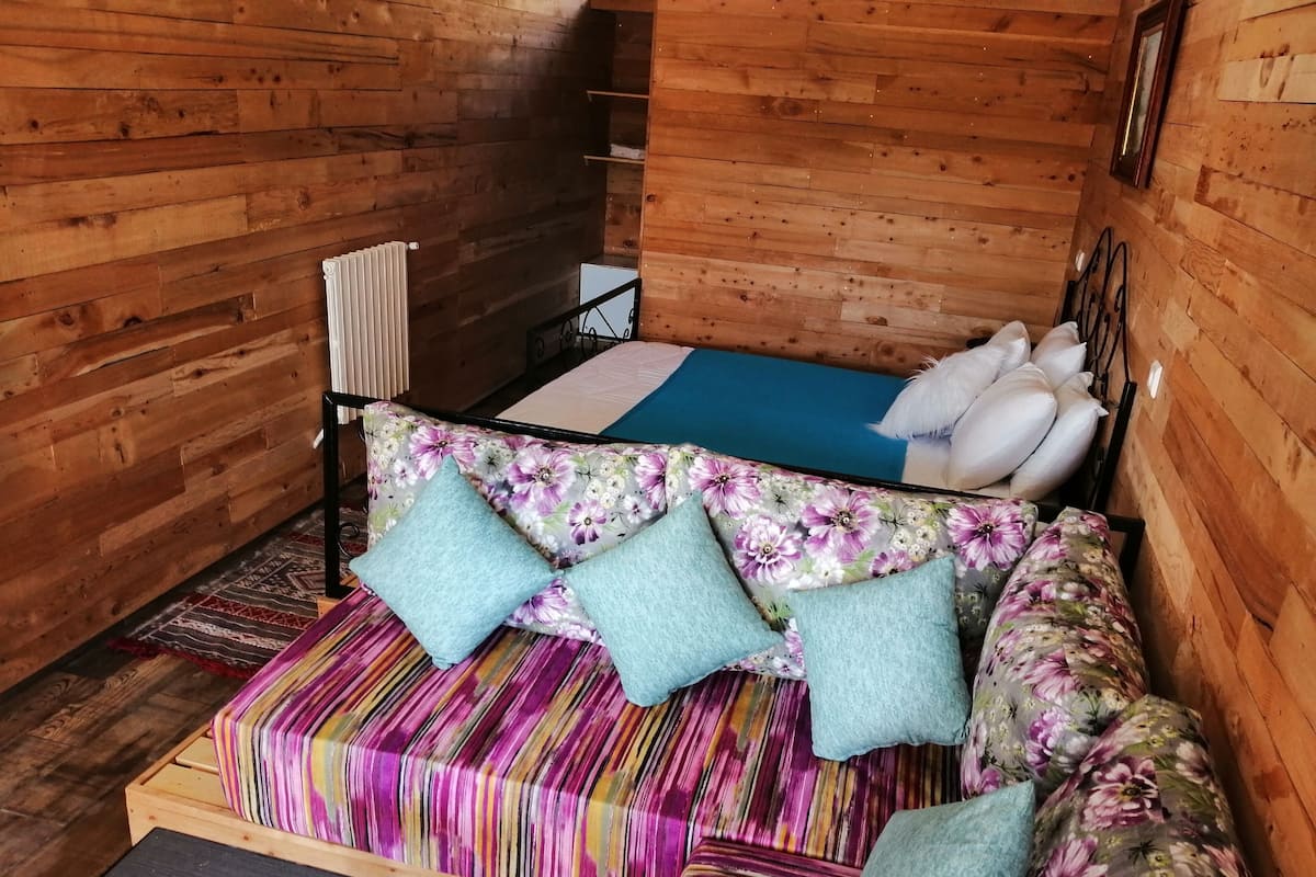 A wooden cabin interior with a sofa bed, a small table, and a radiator.