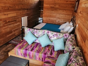 Interior de uma cabana de madeira com sofá-cama, uma mesa pequena e um radiador.