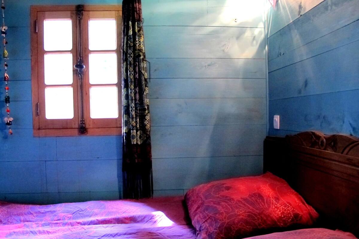 A room with a bed, a window with curtains, and a wall with a wooden door.