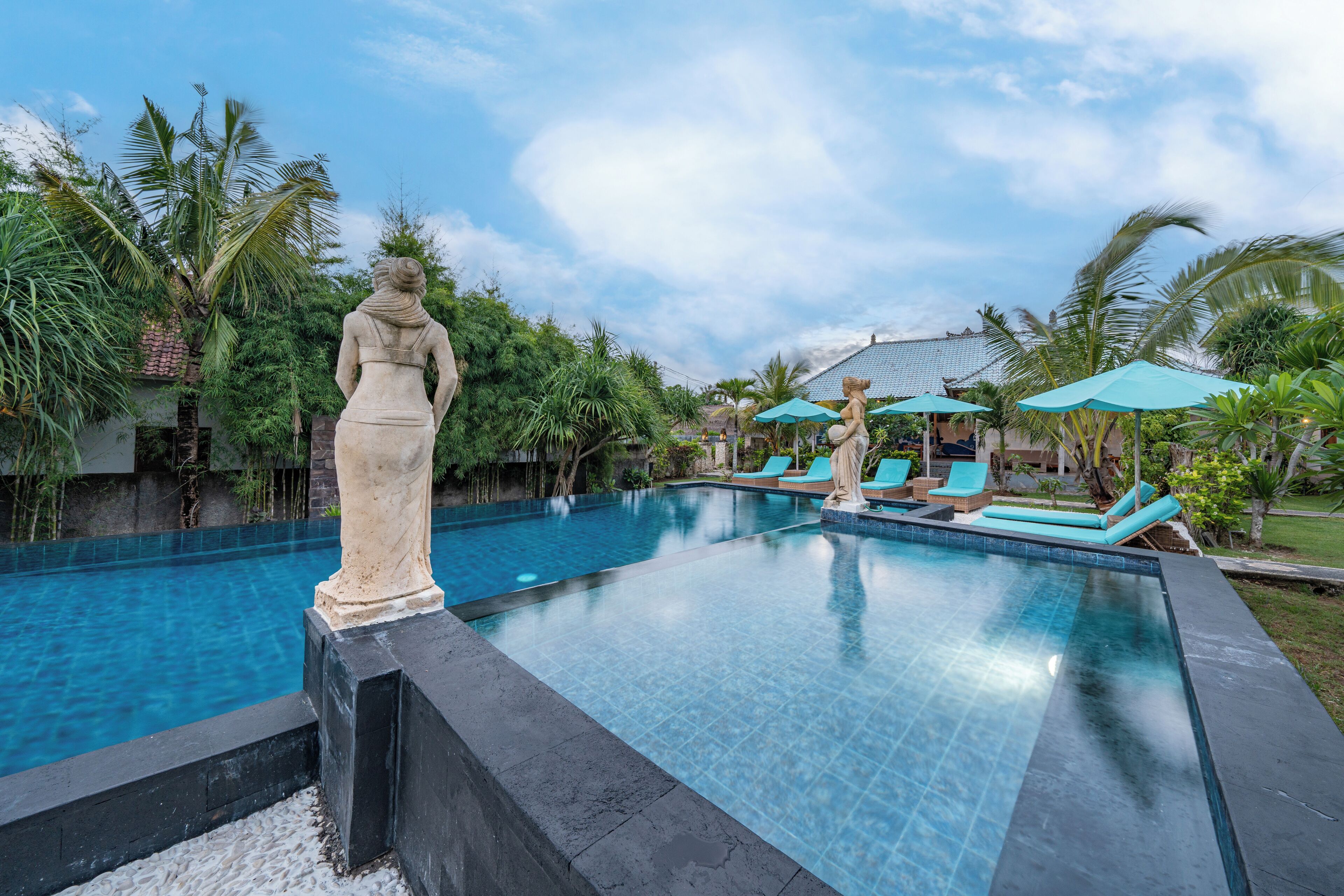 A swimming pool with a statue, lounge chairs, and umbrellas.