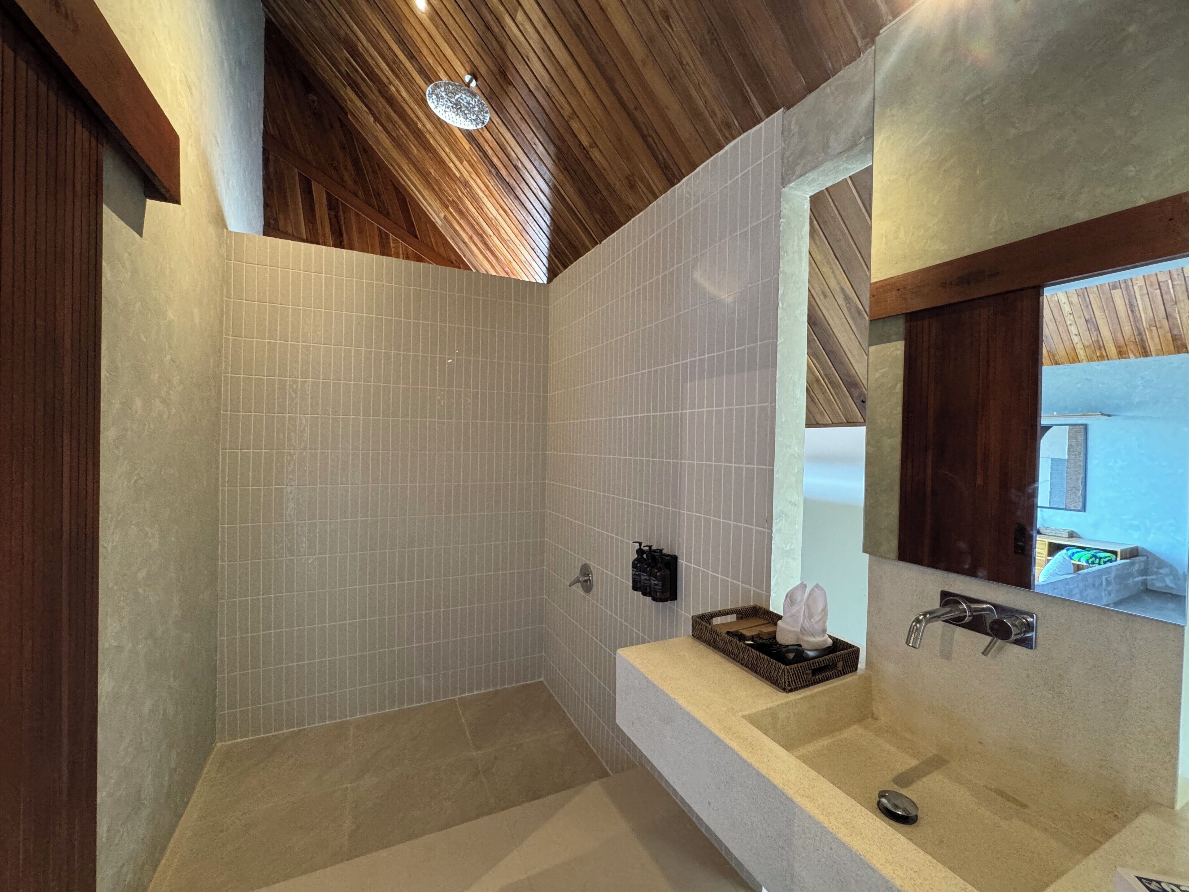 A modern bathroom with a wooden ceiling, tiled walls, a built-in sink, and a shower area.