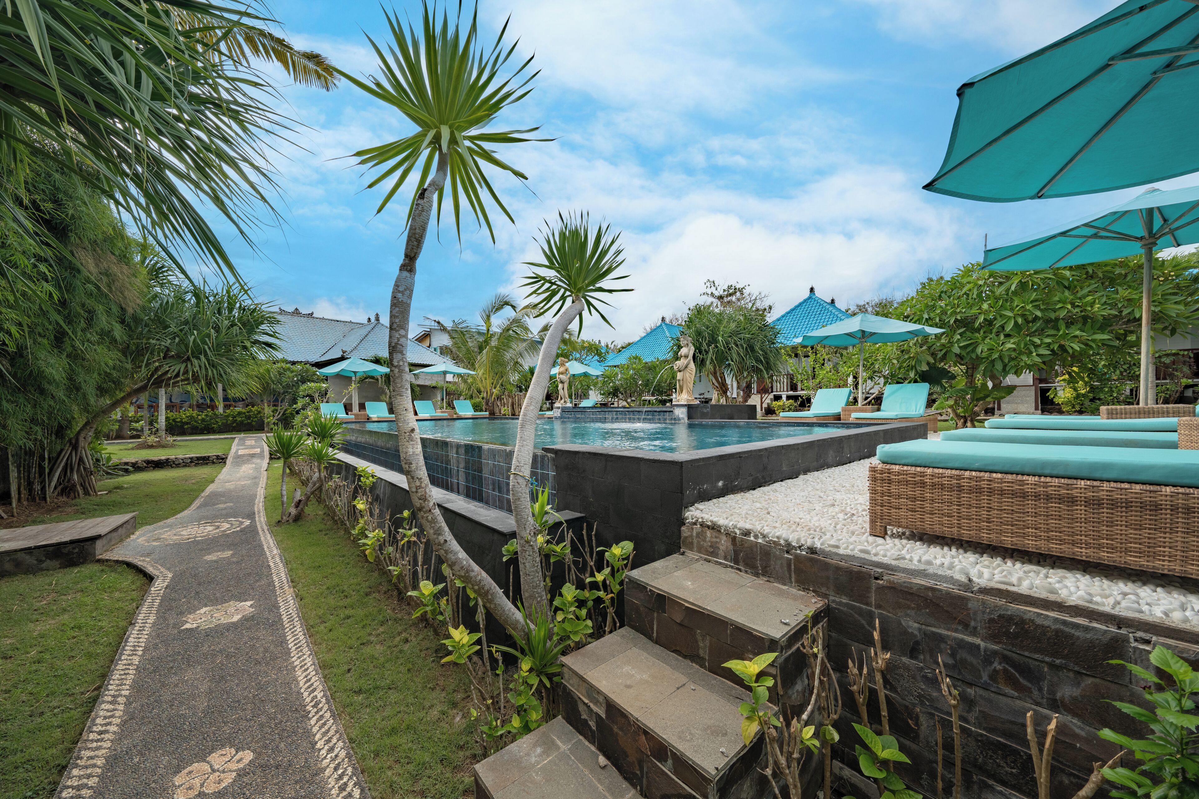 A pool area with lounge chairs, a pathway, and tropical plants.