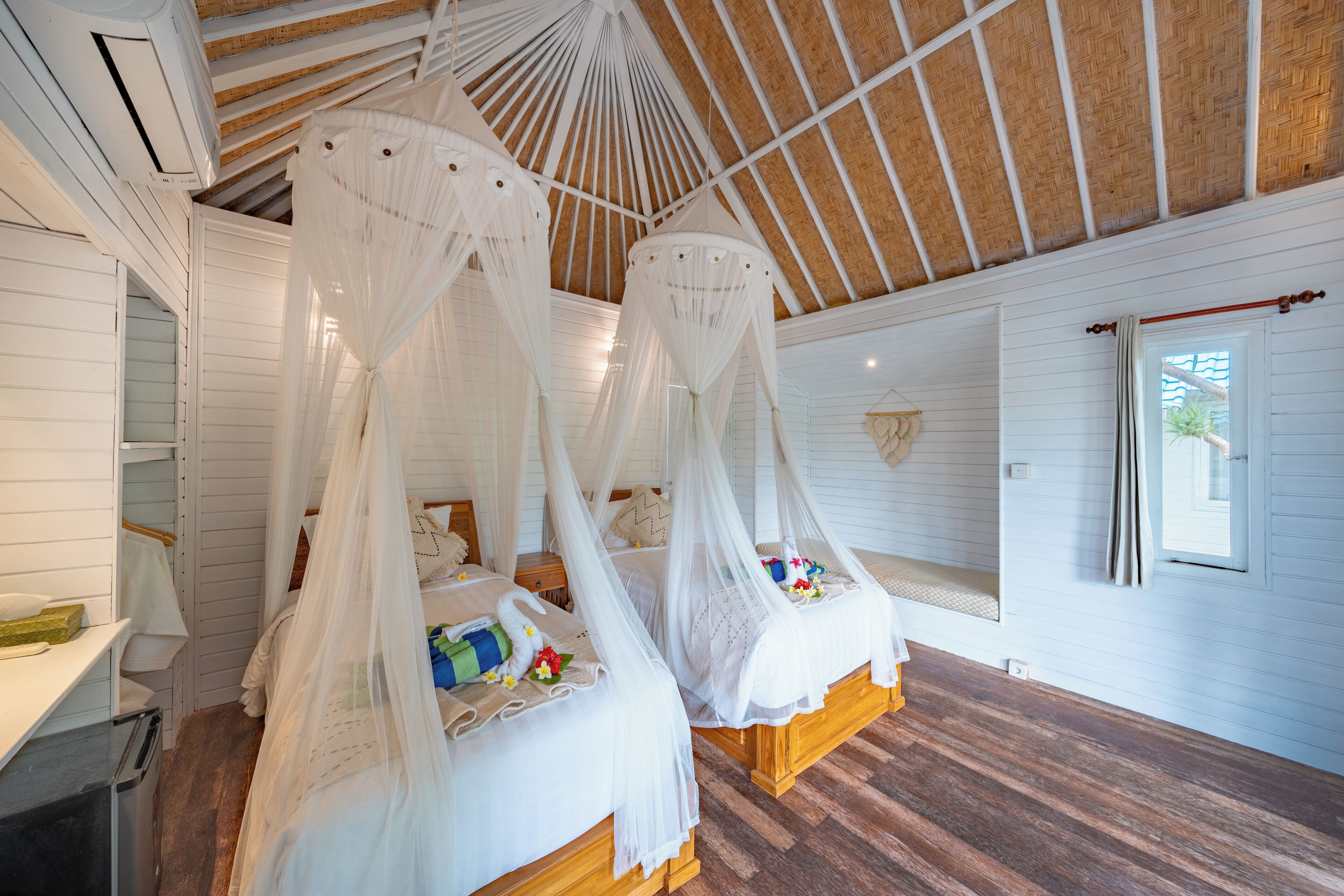 Habitación con dos camas, cada una con dosel, suelo de madera y un ventanal grande.