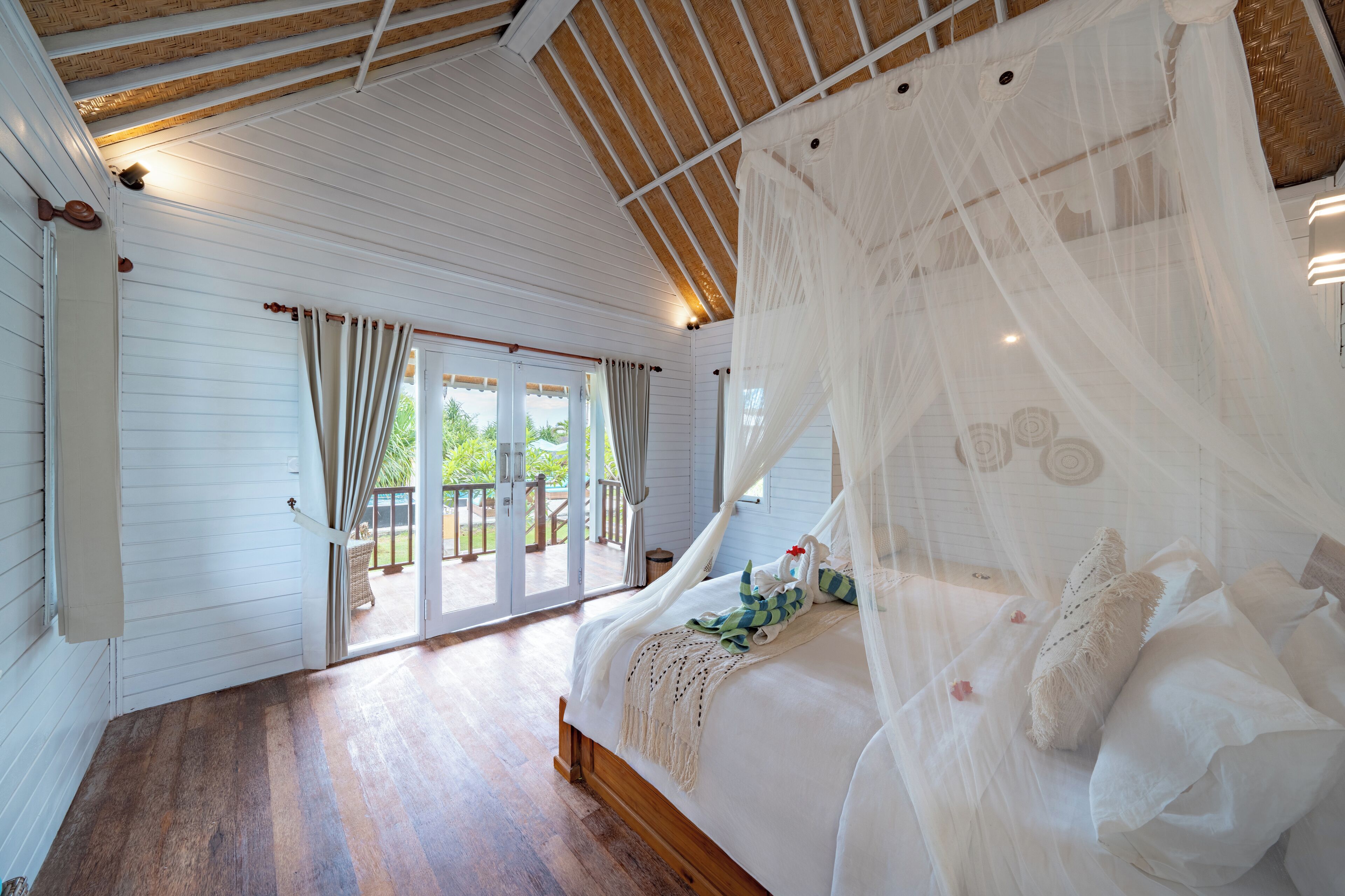 Une chambre à coucher avec un lit à baldaquin, un plancher en bois et une vue sur l’extérieur grâce à une porte-fenêtre coulissante.