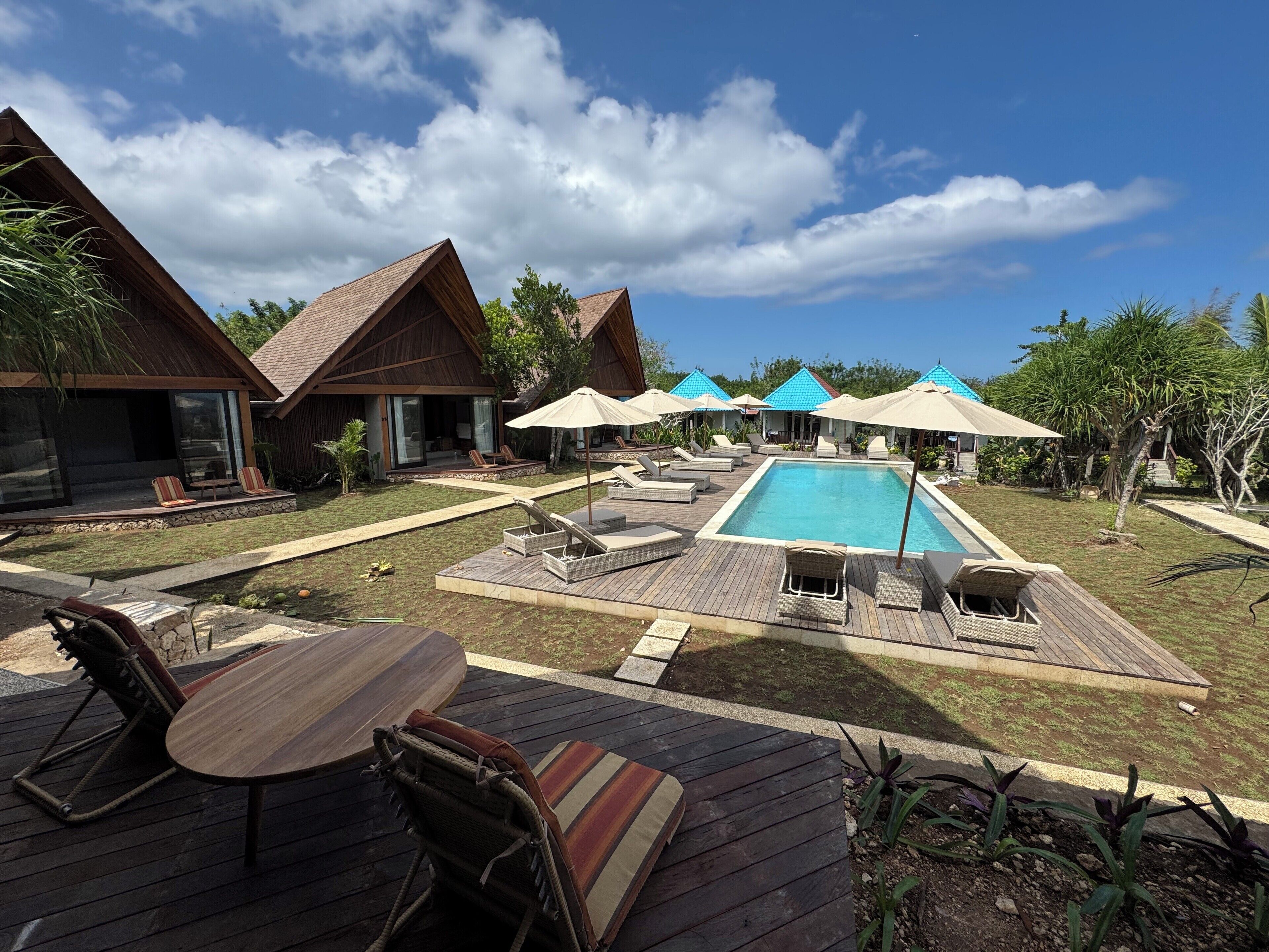 Un espace piscine doté de chaises longues et de parasols, entouré de cabanes en bois avec de grandes fenêtres.