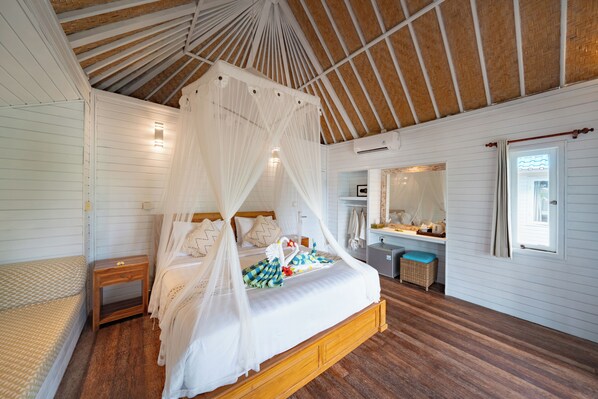 A bedroom with a wooden bed, white bedding, a canopy, a bedside table, a small chair, and a window with curtains.