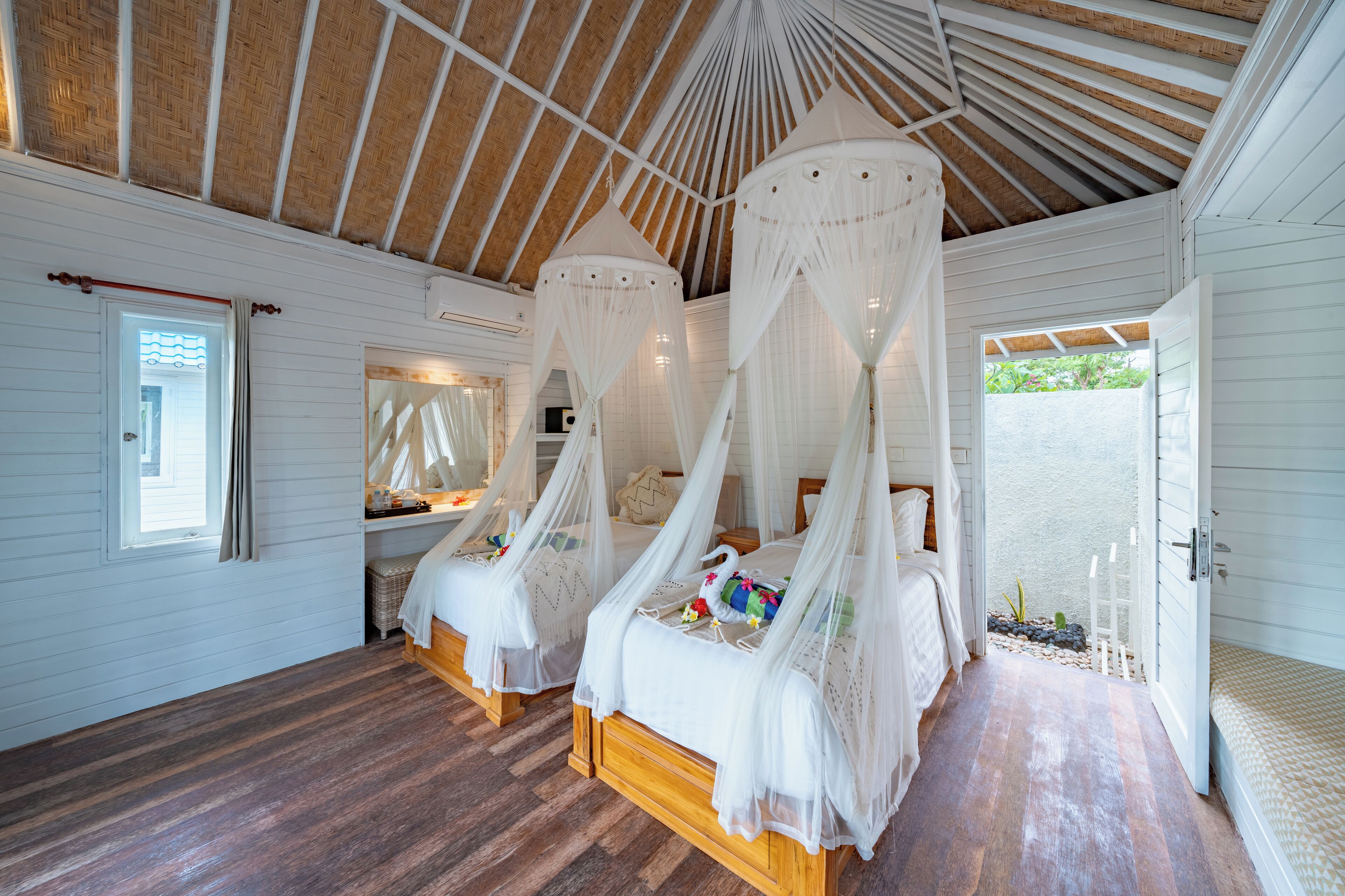 Un dormitorio con dos camas de madera, ropa de cama blanca y una cama con dosel y dosel blanco.