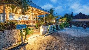 A restaurant with outdoor seating, stone walls, and palm trees. - The Cubang Huts Lembongan (Lembongan Island)