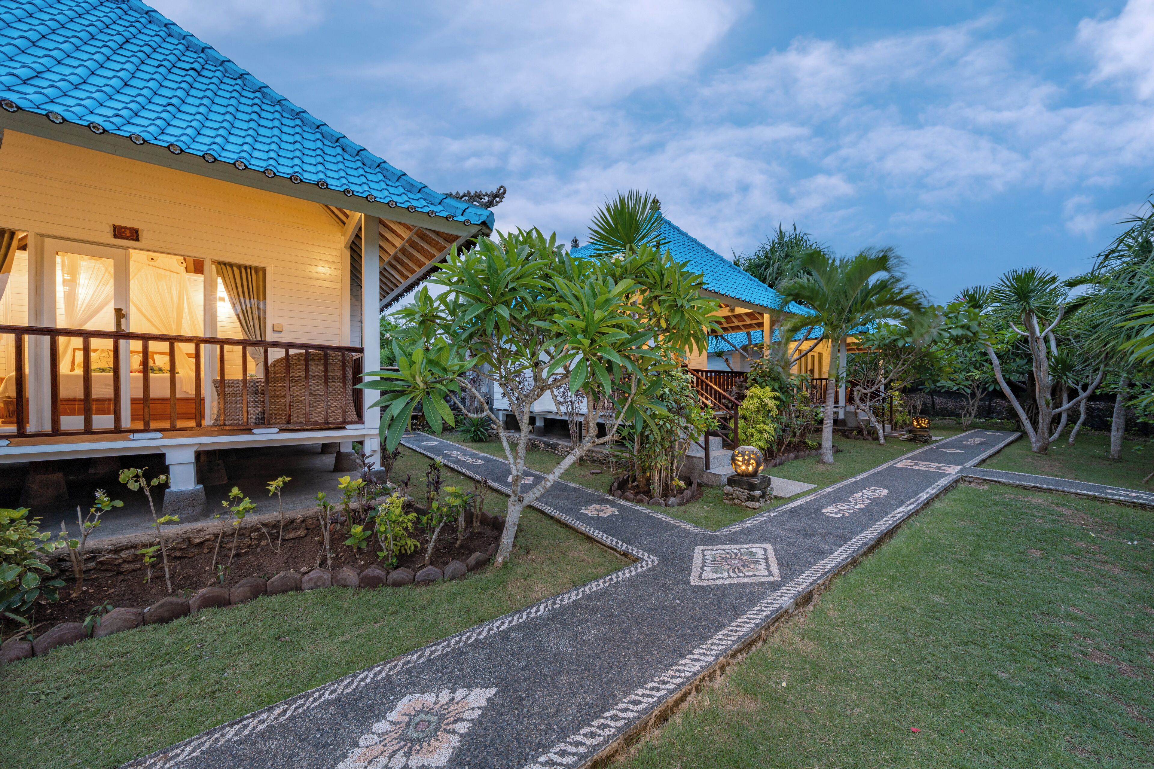 A traditional house with a tiled roof, a paved pathway, and a garden with palm trees.