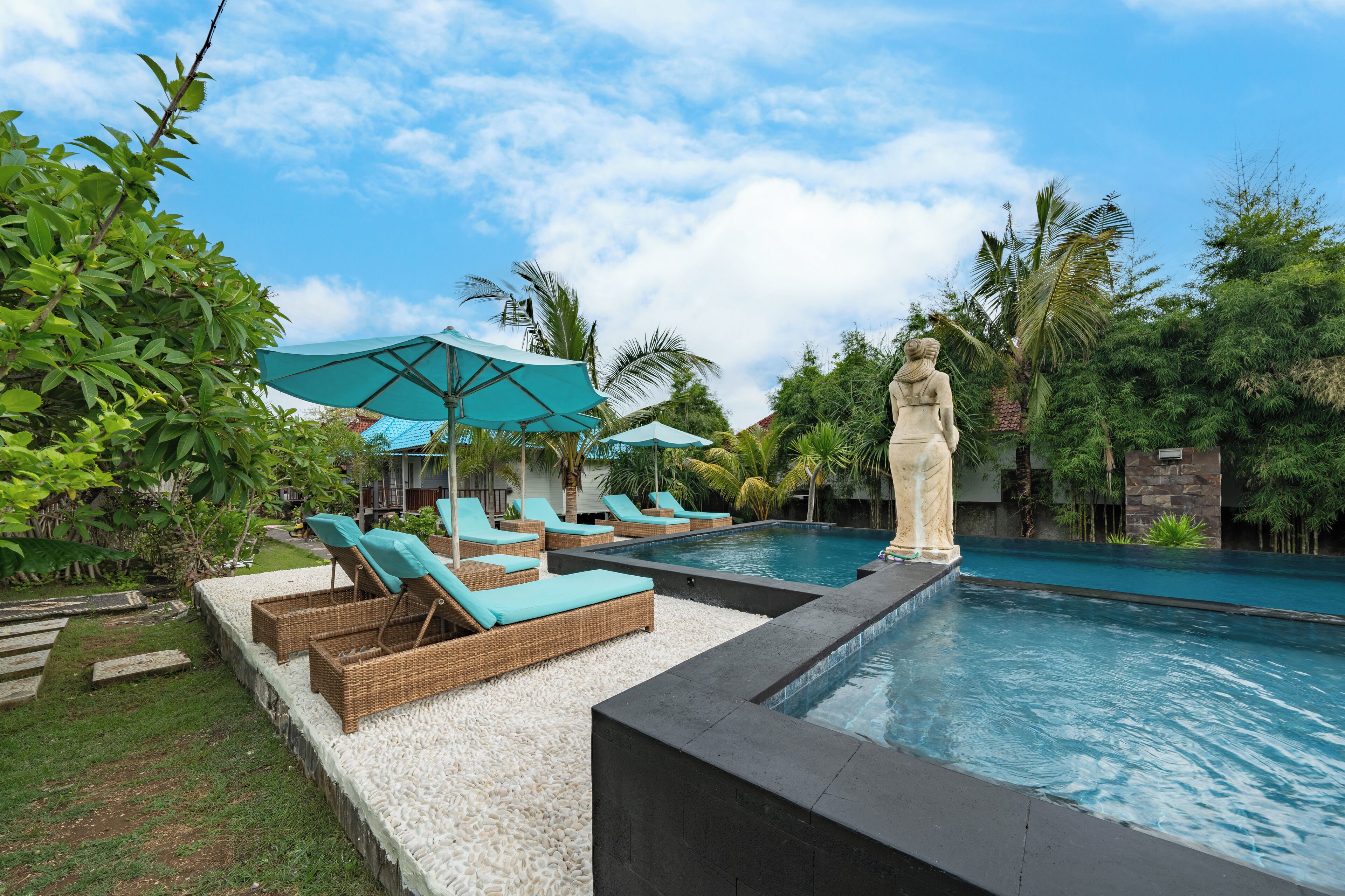 A swimming pool with lounge chairs and umbrellas, surrounded by greenery and a statue.