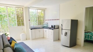 A modern kitchen with white cabinets, a refrigerator, and a microwave. There is a sofa with cushions in the living area. - Casa Eco | Private Apartment In Taganga | 600 Meters away from beach (Taganga)