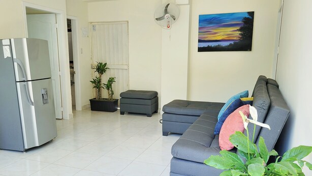 A living room with a grey sofa, a white refrigerator, a potted plant, and a painting on the wall. - Casa Eco | Private Apartment In Taganga | 600 Meters away from beach (Taganga)