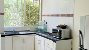 A kitchen with white cabinets, a black countertop, a window with a view of greenery, a microwave, and a refrigerator. - Casa Eco | Private Apartment In Taganga | 600 Meters away from beach (Taganga)
