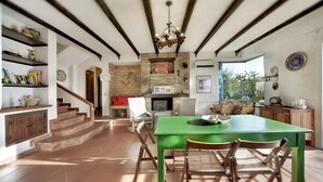 Una cocina amplia con una mesa verde y sillas de madera, una chimenea de piedra y una escalera que sube a otro nivel.