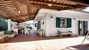 Un patio al aire libre con una pérgola de madera, una mesa con sillas y un banco de piedra.