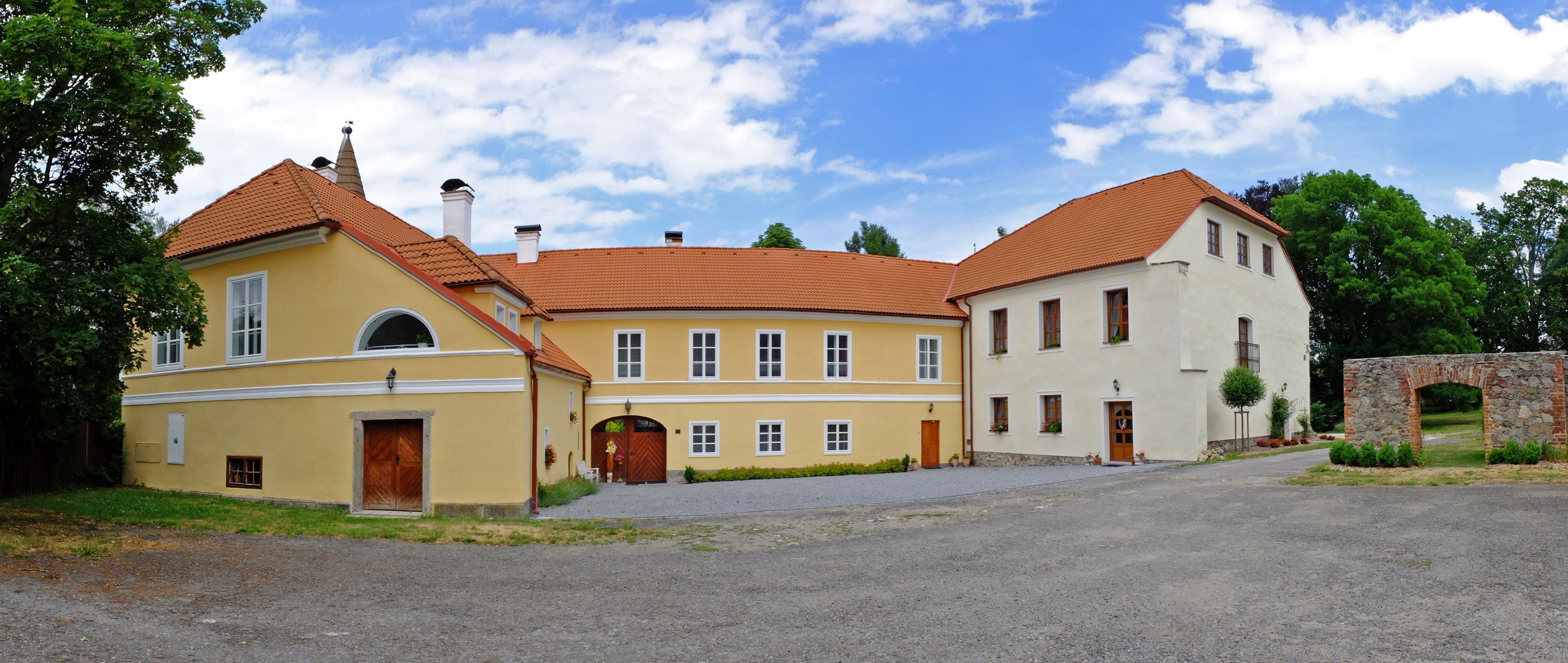 A two-story building with a yellow facade and a red-tiled roof, featuring a stone archway and a gravel driveway.