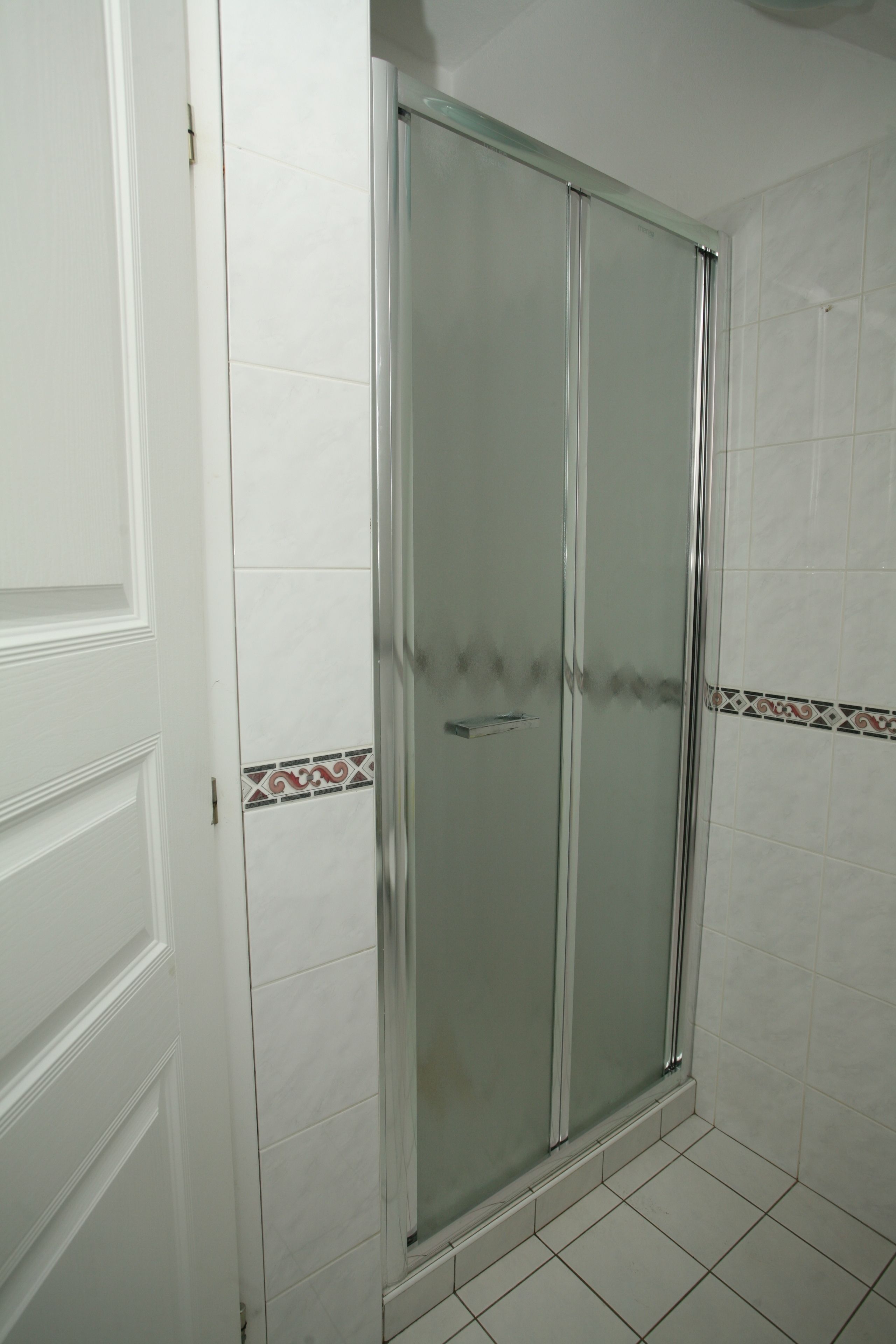 Un baño con cabina de ducha de vidrio, paredes de azulejos blancos y una puerta con panel decorativo.