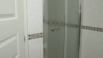 Un baño con cabina de ducha de vidrio, paredes de azulejos blancos y una puerta con panel decorativo.