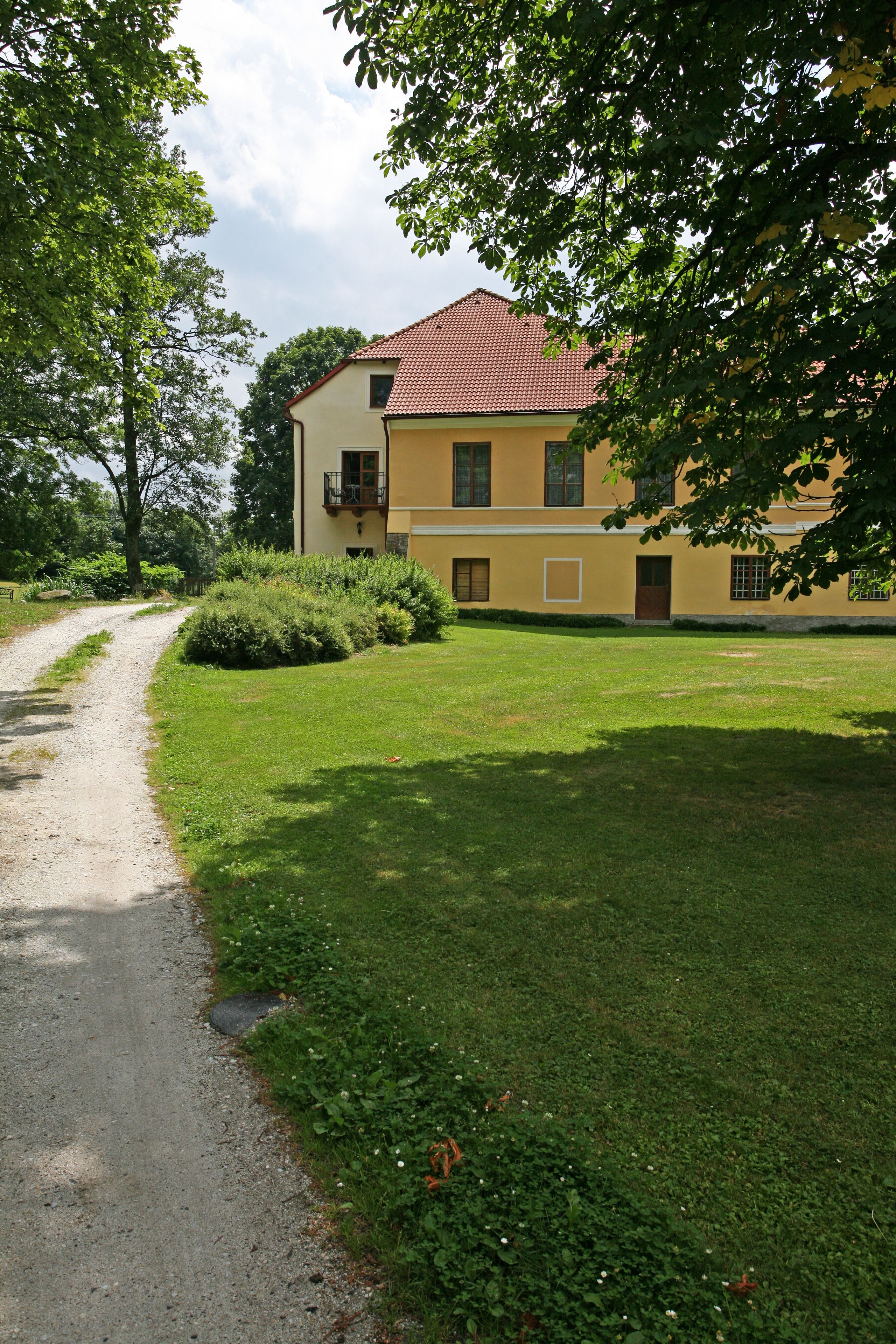 A yellow building with a red roof, a gravel path, and green grass.