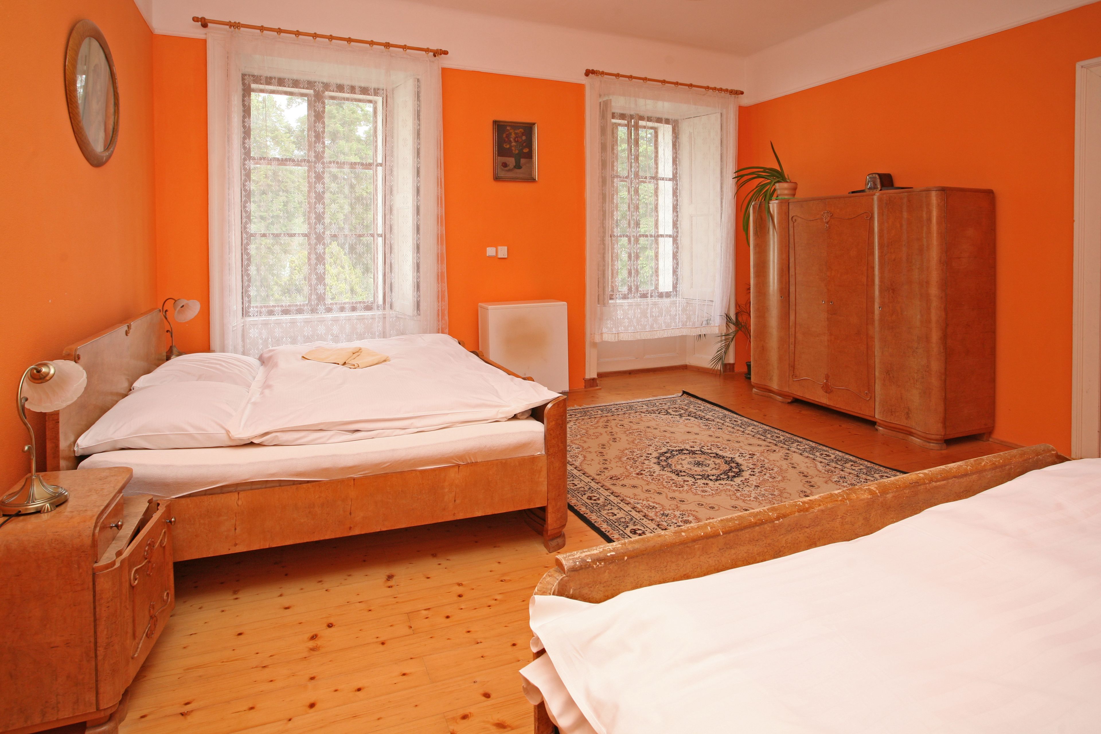 A bedroom with two beds, a wooden wardrobe, a desk with a lamp, and a window with curtains.