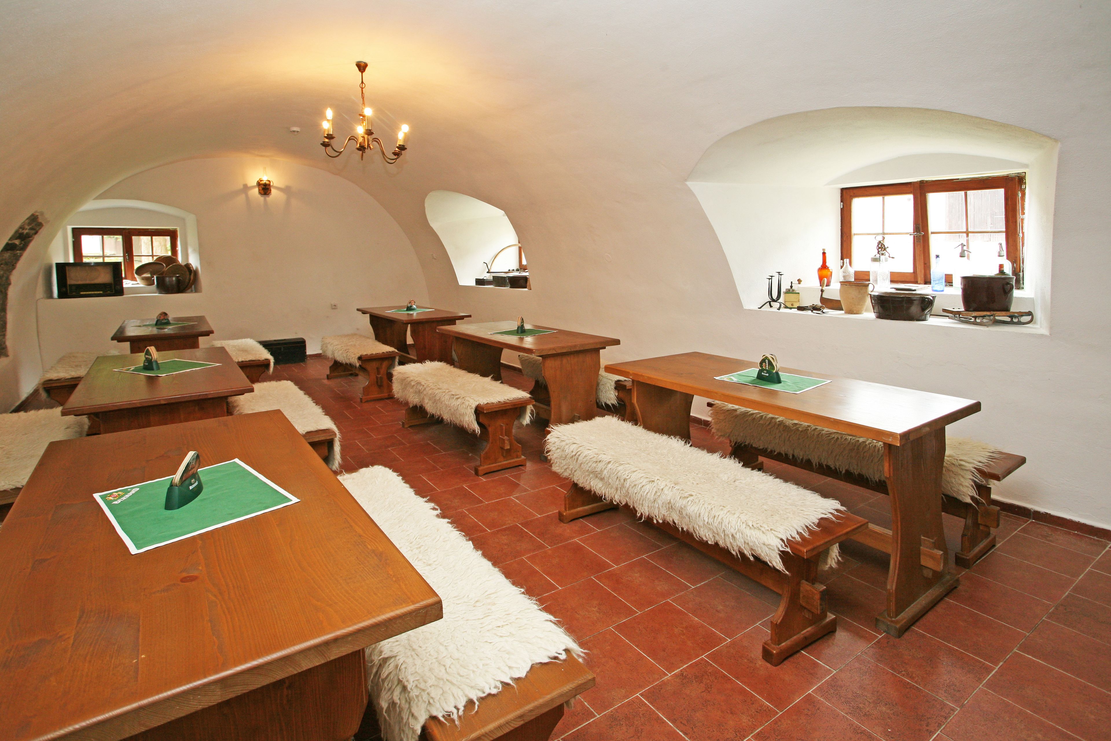 A dining area with wooden tables and benches, a chandelier, and a window with kitchen items.