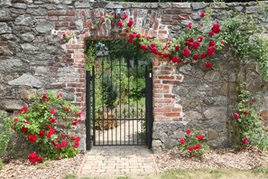 Un arco de piedra con un portón negro, rodeado de rosales rojos y follaje.