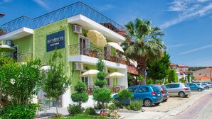 Un hôtel à la façade verdoyante, doté de balcons ornés de parasols et d’une rangée de voitures garées.