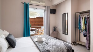 Une chambre d’hôtel comprenant un lit, une petite table, un téléviseur, une armoire et un balcon doté d’un plancher en bois.