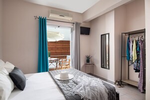 A hotel room with a bed, a small table, a TV, a wardrobe, and a balcony with wooden flooring.