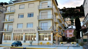 Un hotel de varios pisos llamado "HOTEL BRISTOL" con balcones, un restaurante en la planta baja y mesas al aire libre.