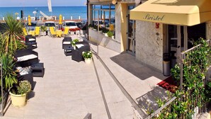 Un hotel frente al mar con terraza exterior, un toldo amarillo y vistas al océano.