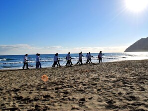 A beach scene with people walking along the shore, a clear sky, and a distant cliff. - Hotel Bristol (Laigueglia)