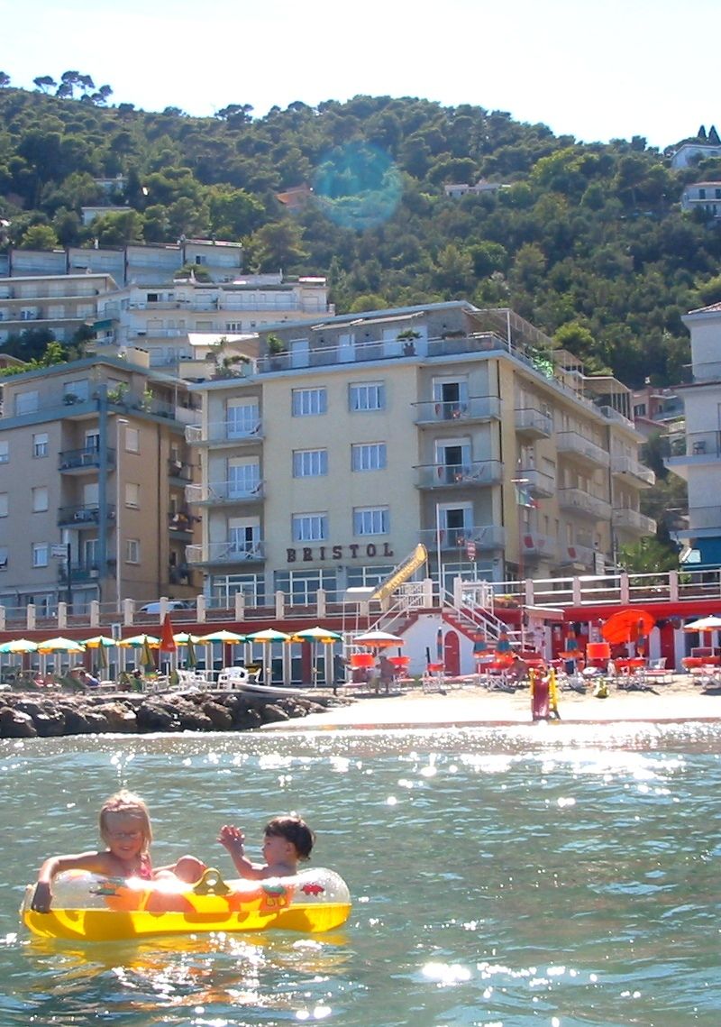 A coastal hotel with multiple floors, balconies, and a beach area with umbrellas.