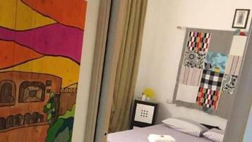 Een slaapkamer met een bed, een nachtkastje, een stoel en een muur met een kleurrijk schilderij.