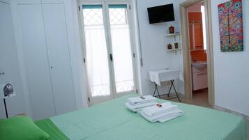 A hotel room with a green bedspread, white walls, a TV mounted on the wall, and a bathroom visible through an open door.