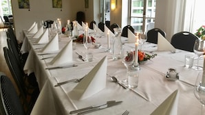 A long dining table set with white tablecloths, candles, and glassware, with chairs aligned on both sides.