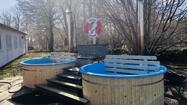 A wooden deck with two hot tubs, a wooden bench, and a sign with text.