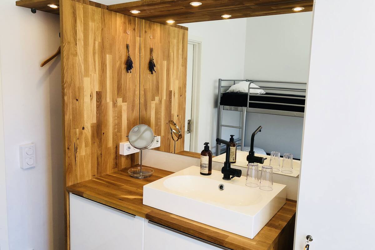 A modern bathroom with a wooden vanity, a large mirror, a white sink, and a built-in bench.