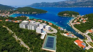 An aerial view of a coastal town with buildings, a tennis court, and a bay with boats. - White Cloud Apartments (Korcula)